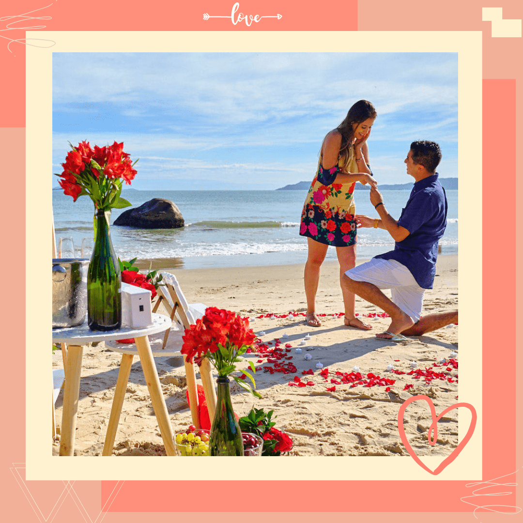 homem ajoelhado pedindo sua amada em namoro na praia sobre a areia perto do mar com flores pelo chão