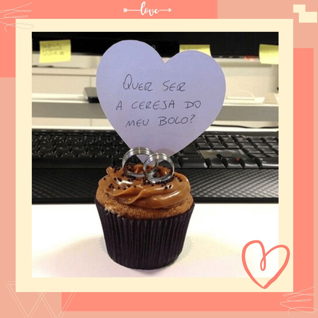 duas alianças em cima de um cupcake e uma frase escrita em um coração de papel