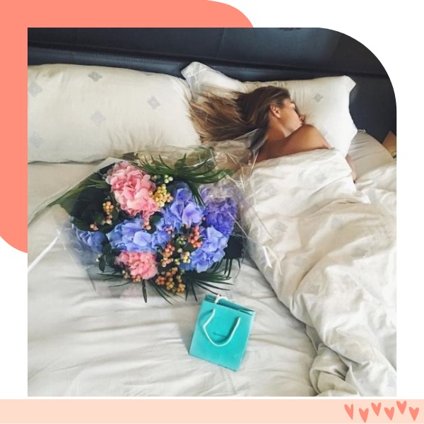 moça deitada na cama e buque de flores ao lado